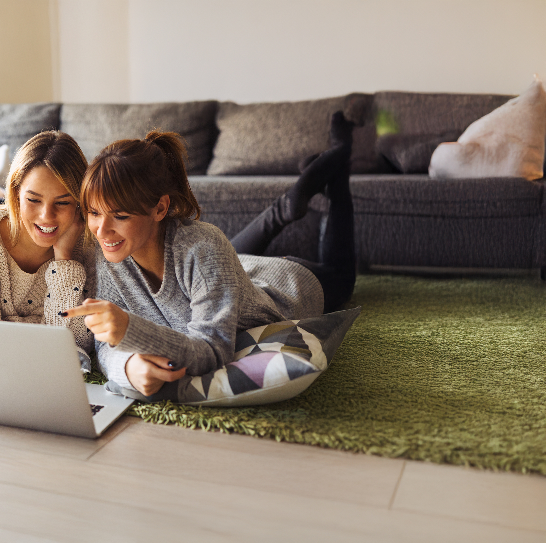 Zwei Frauen liegen entspannt vor einem Laptop und schauen gemeinsam darauf.