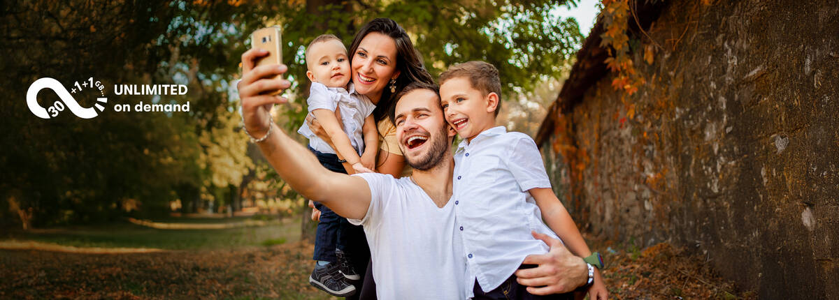Unbegrenztes Datenvolumen: Vater macht ein Selfie von Familie vor einem Baum.