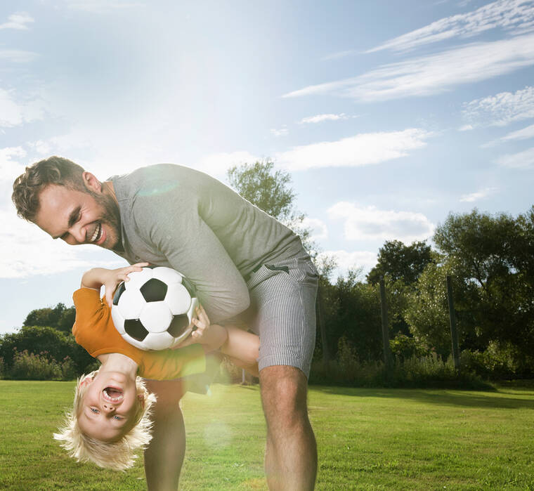 Ein Mann hebt einen Jungen hoch der einen Fußball in der Handy hält