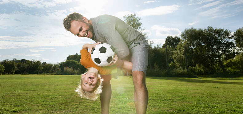 Ein Mann hebt einen Jungen hoch der einen Fußball in der Handy hält