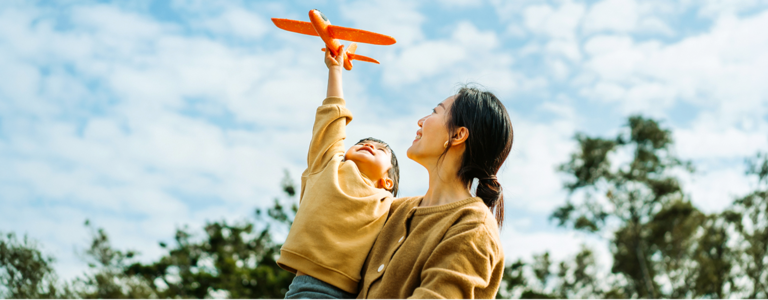Mutter hat Kind auf dem Arm das ein Spielzeugflugzeug fliegen lässt