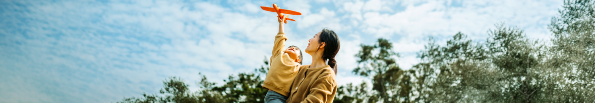 Mutter hat Kind auf dem Arm das ein Spielzeugflugzeug fliegen lässt