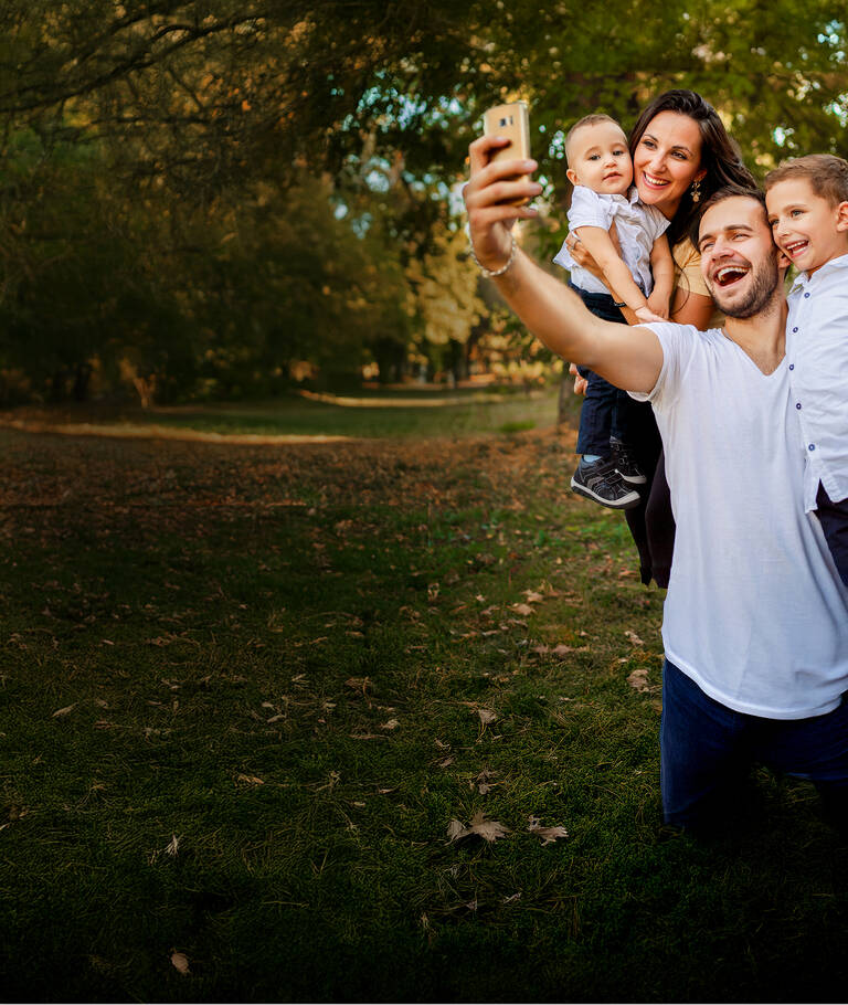 Unbegrenztes Datenvolumen: Vater macht ein Selfie von Familie vor einem Baum.