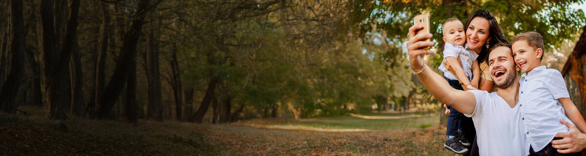 Unbegrenztes Datenvolumen: Vater macht ein Selfie von Familie vor einem Baum.